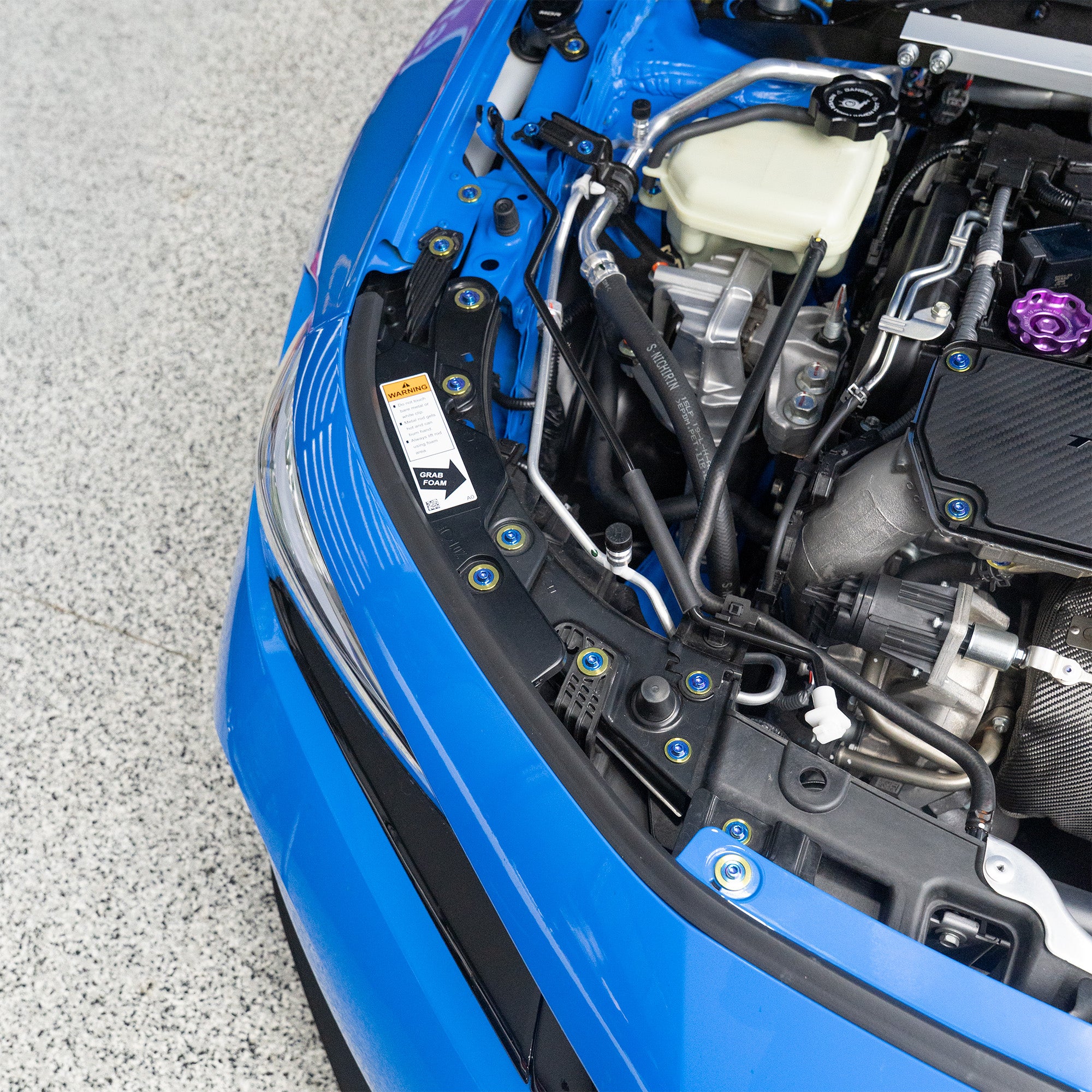 Close-up of a blue car's open hood revealing the engine and titanium hardware