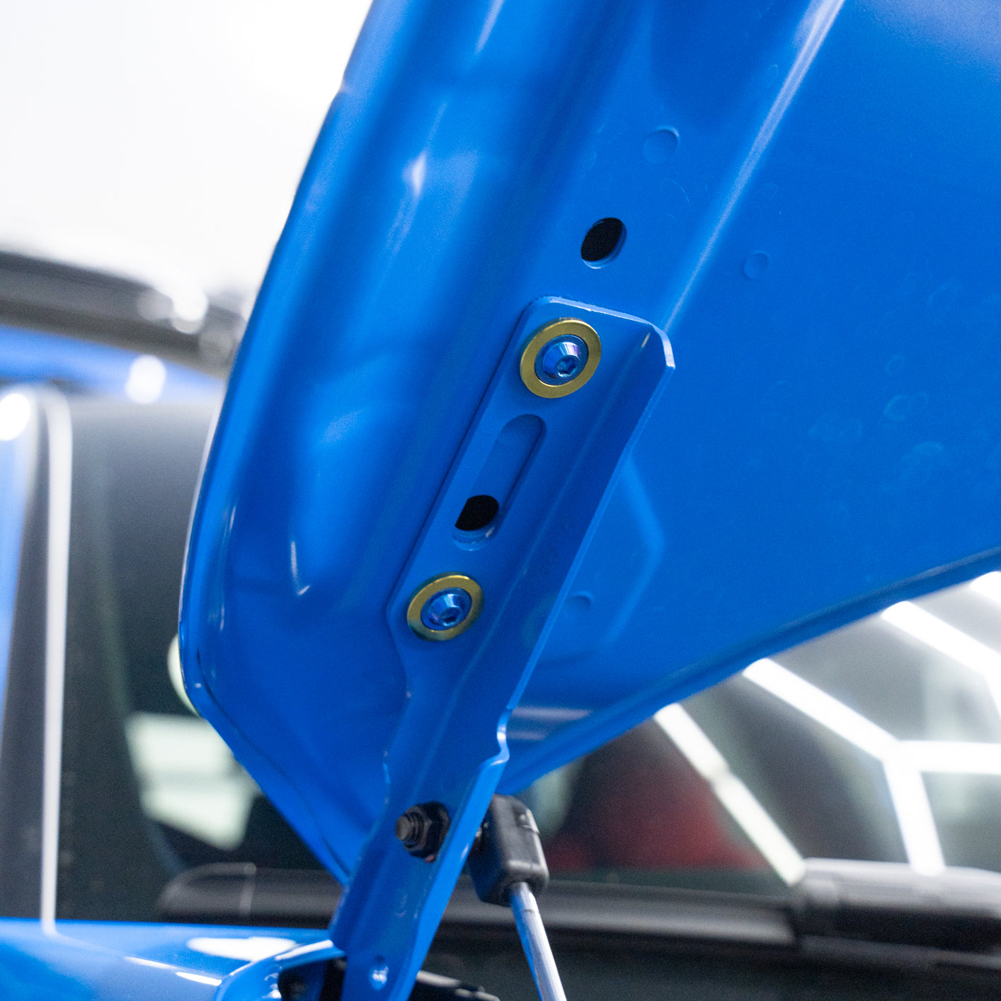 Close-up of a blue car part with titanium screws on a blurred background