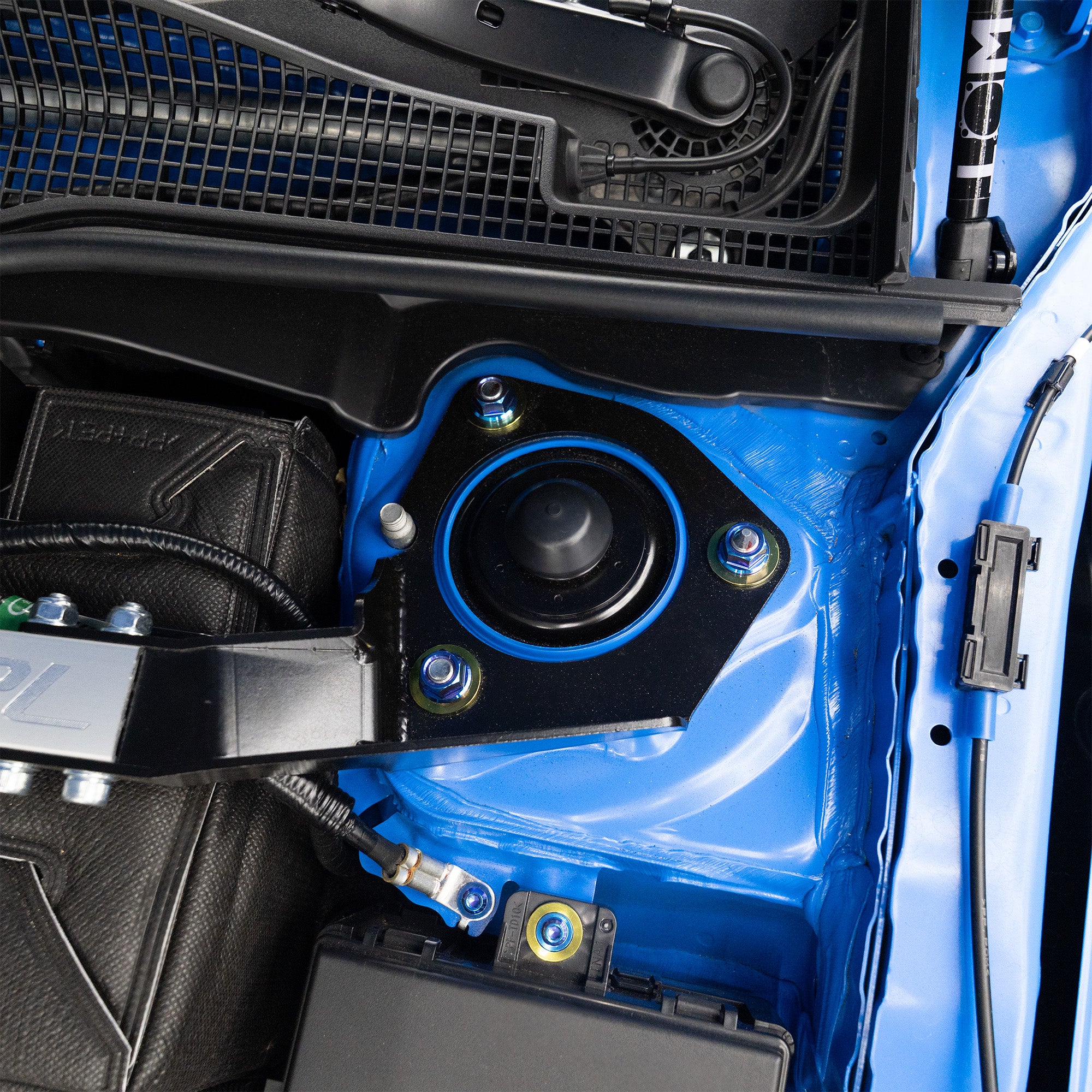 Close-up of a blue car engine bay with titanium strut tower nuts and washers