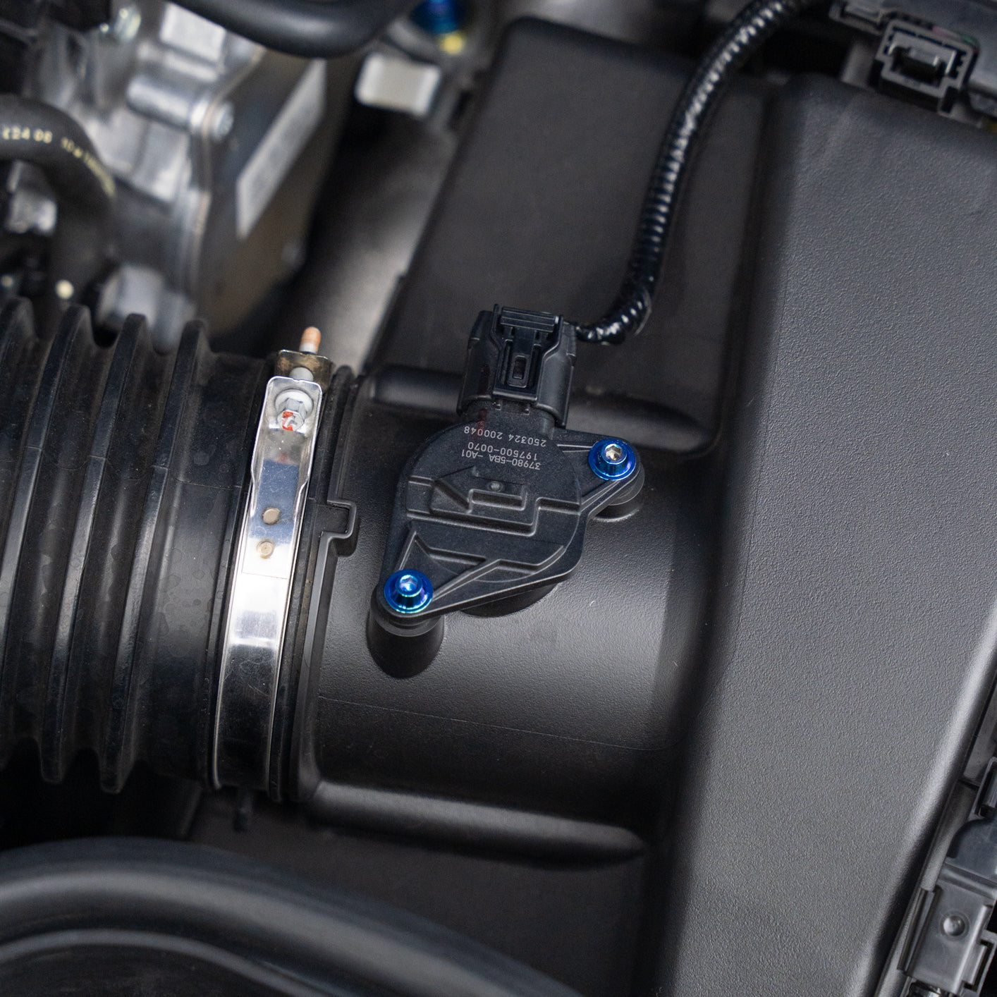 Close-up of a car's air intake system with a black plastic MAF sensor and blue titanium screws.