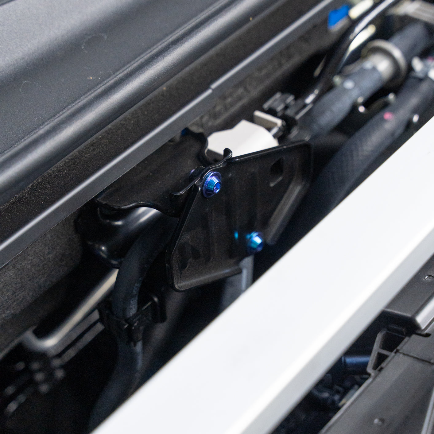 Close-up of a vehicle's mechanical components and a black bracket with blue titanium hardware.