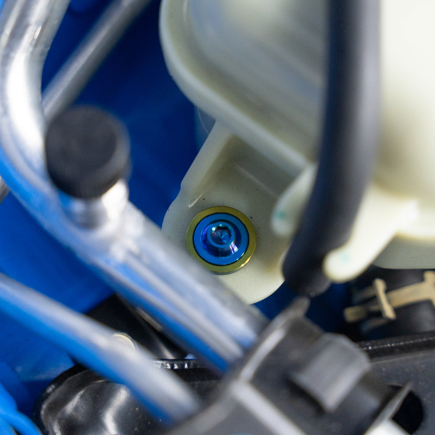 Close-up of a blue and gold titanium bolt on a coolant reservoir.