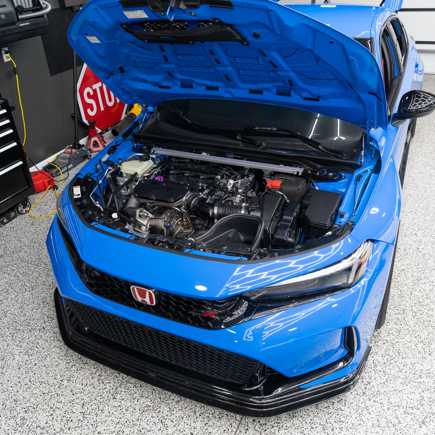 Blue car with open hood in a garage setting showing off its titanium hardware.