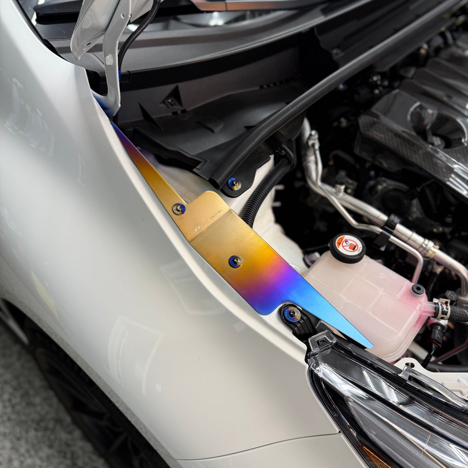 JDC Titanium fender shroud for 2023-2025 Toyota GR Corolla in a burnt gradient finish with matching titanium hardware installed on a white GR Corolla.