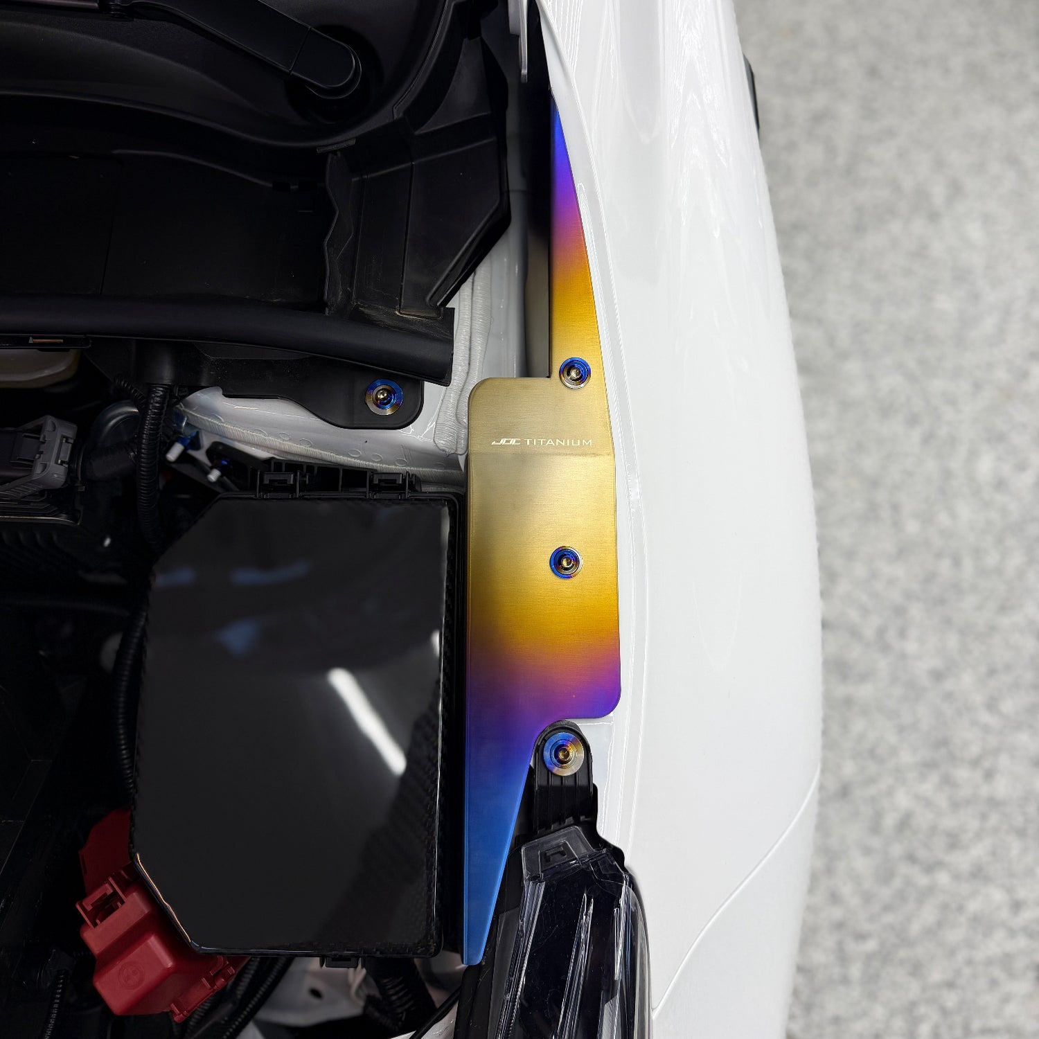 JDC Titanium fender shroud for 2023-2025 Toyota GR Corolla in a burnt gradient finish with matching titanium hardware installed on a white GR Corolla.