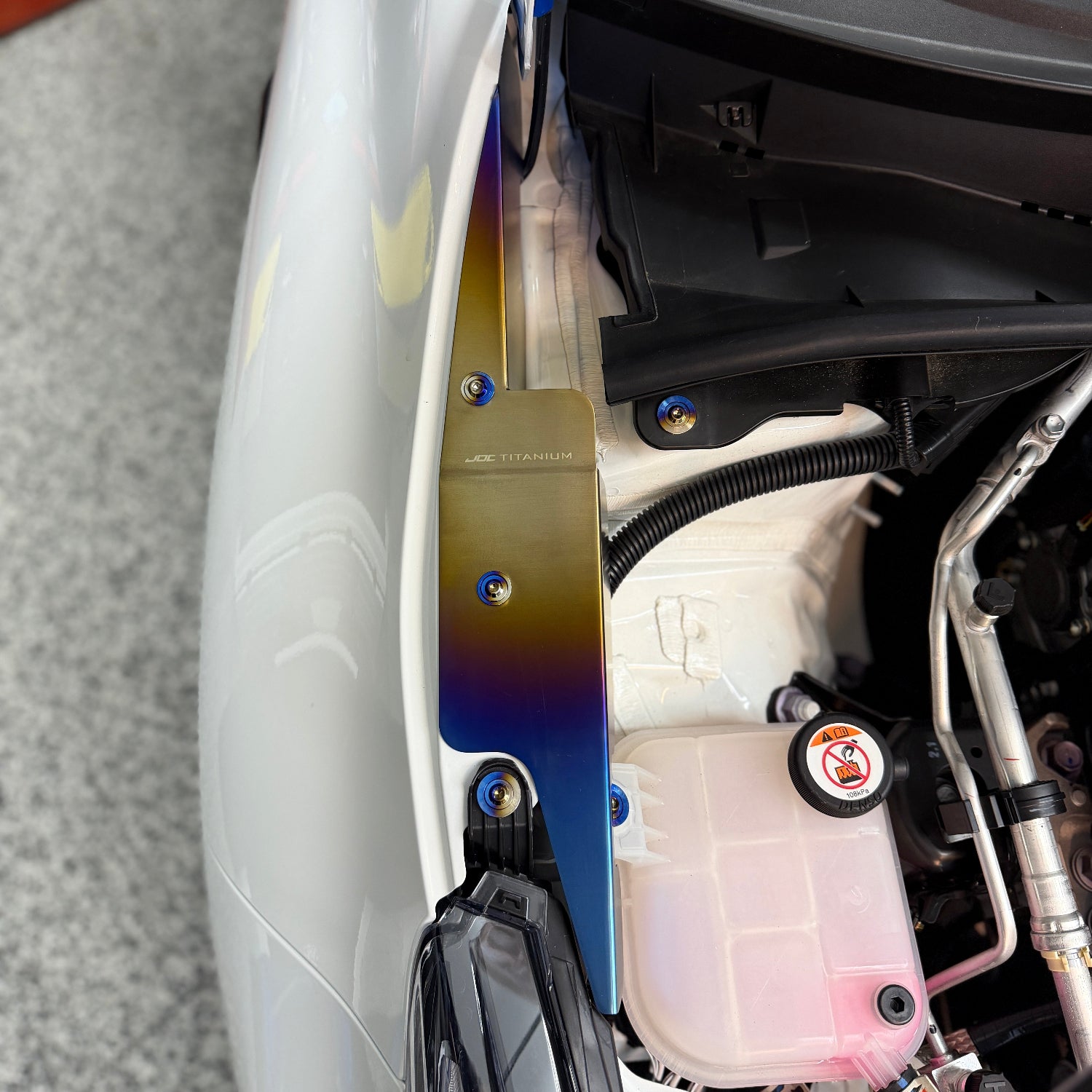 JDC Titanium fender shroud for 2023-2025 Toyota GR Corolla in a burnt gradient finish with matching titanium hardware installed on a white GR Corolla.