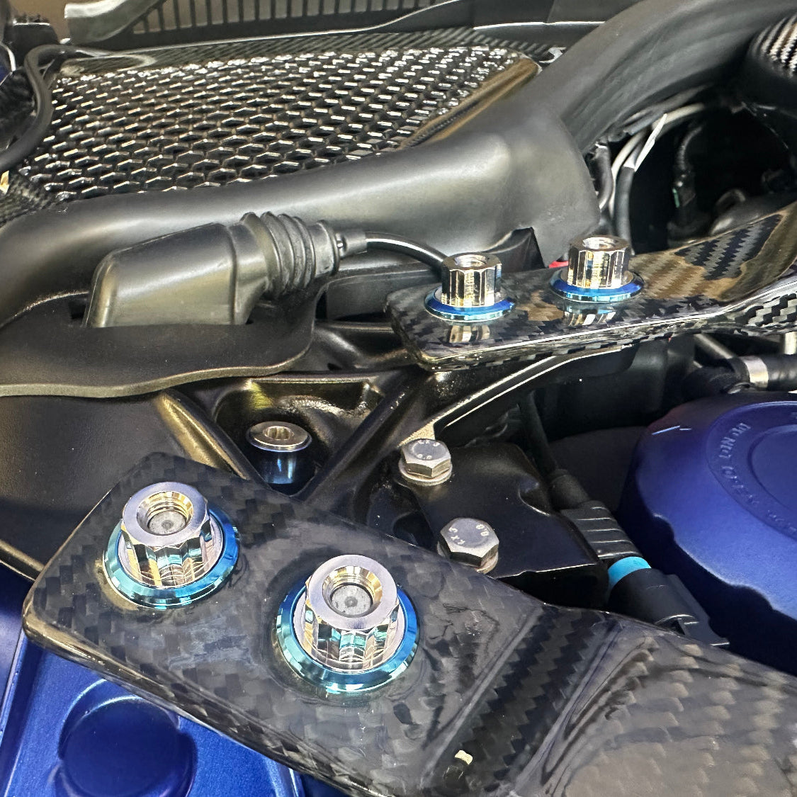 Close-up of a car engine with various components and blue titanium fasteners.