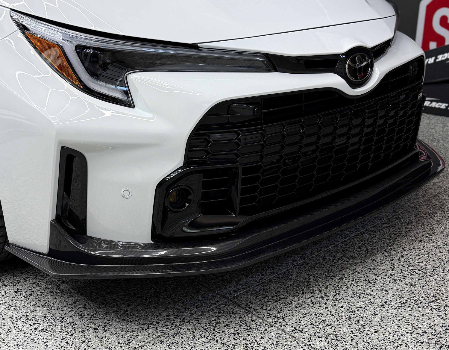 Rexpeed carbon fiber V1 front splitter for 2023-2024 Toyota GR Corolla installed on a white car.