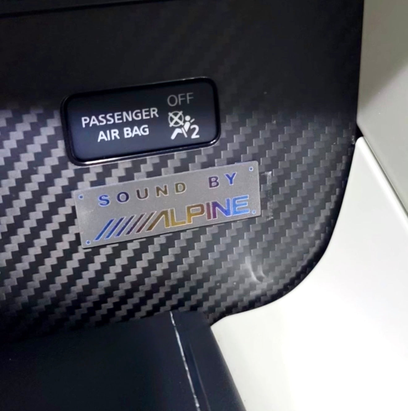Car interior with a passenger airbag indicator and an Alpine sound system badge.