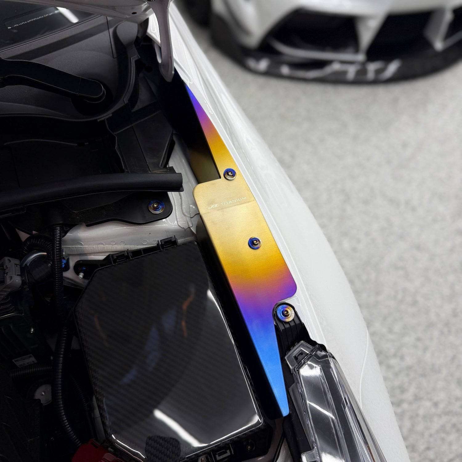 JDC Titanium fender shroud for 2023-2025 Toyota GR Corolla in a burnt gradient finish with matching titanium hardware installed on a white GR Corolla.