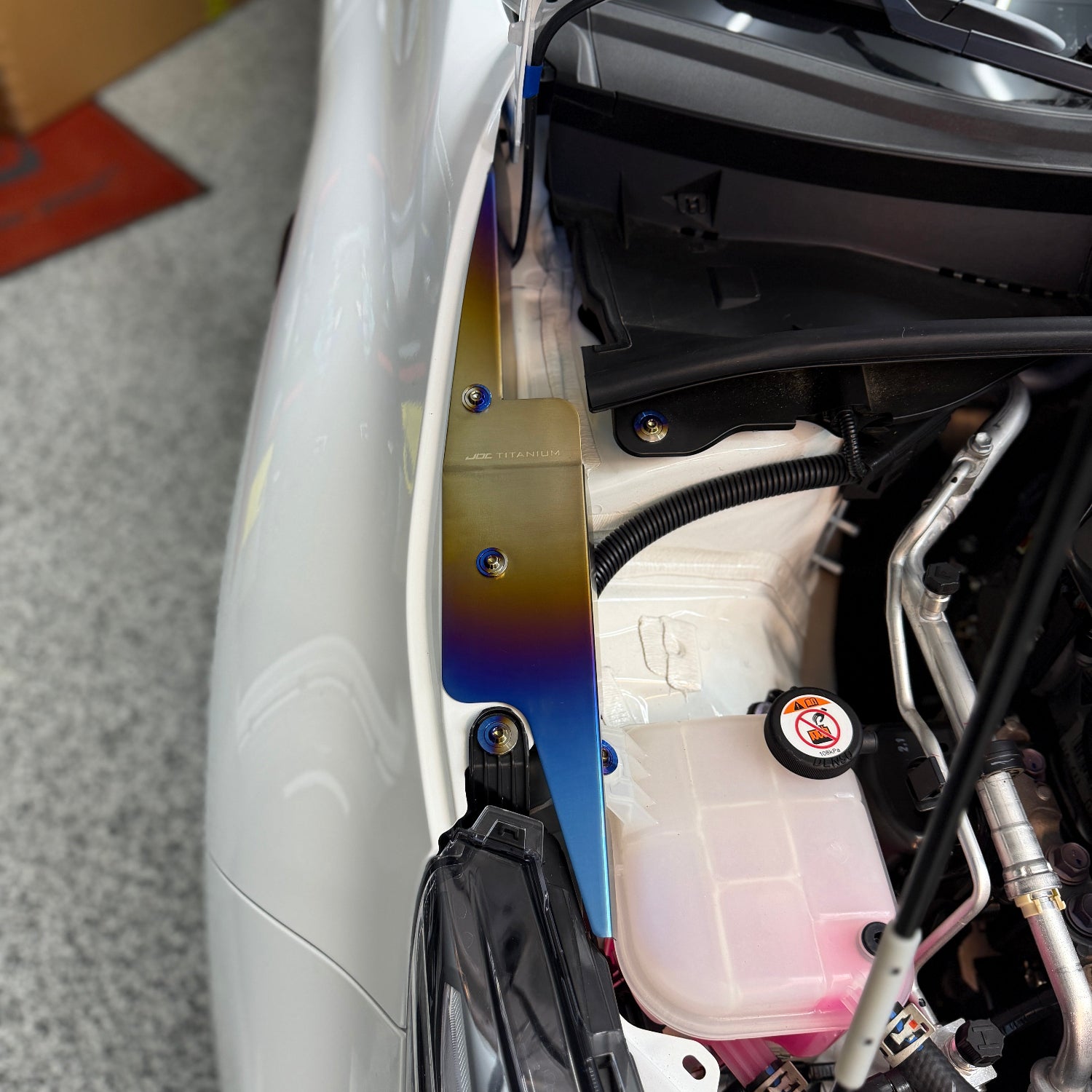 JDC Titanium fender shroud for 2023-2025 Toyota GR Corolla in a burnt gradient finish with matching titanium hardware installed on a white GR Corolla.