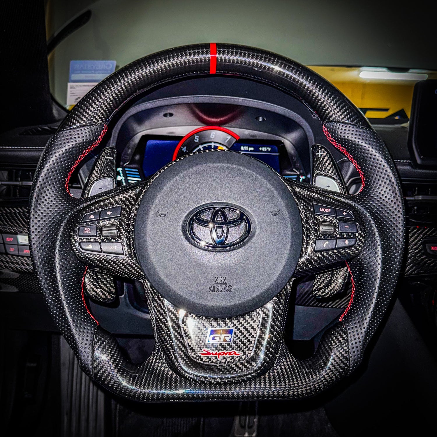 JDC Titanium GR Steering Wheel Badge in a burnt gradient finish installed on a carbon fiber steering wheel on a A90 Supra