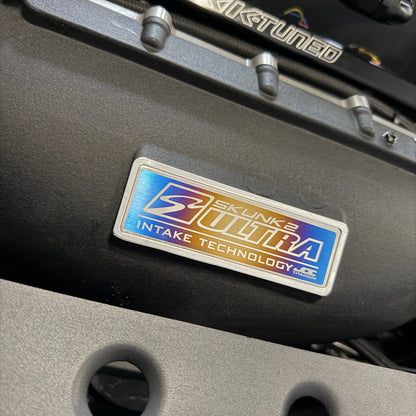 Close up of the JDC Titanium Skunk2 intake manifold badge installed on a black intake manifold.