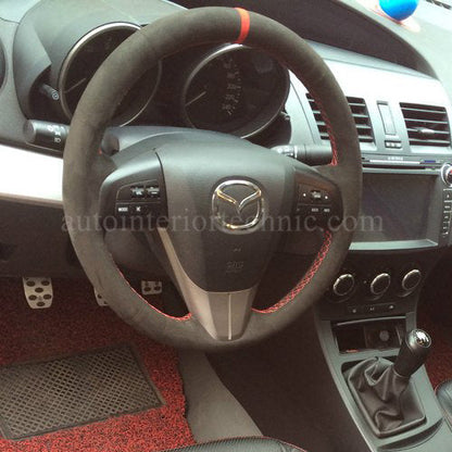 Car interior with steering wheel and dashboard, featuring a Mazda logo.